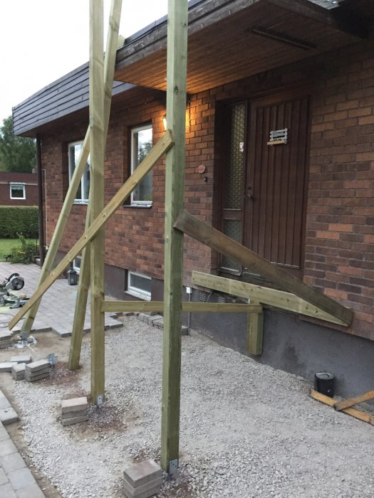 Pågående konstruktion av en trätrappa och ramp, med stödstolpar och bärlina i fasad.