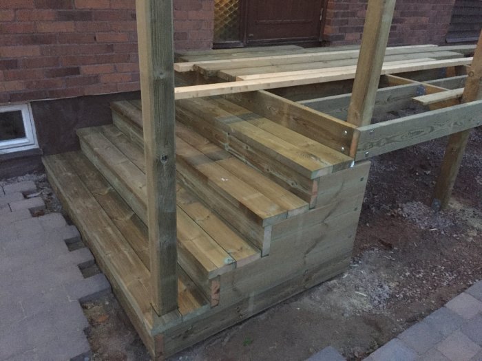 En nybyggd trätrappa och barnvagnsramp utanför ett hus i skymningen.