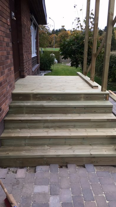 Nybyggd trätrappa och plattform utanför en tegelhusfasad, med pågående byggnadsarbete.