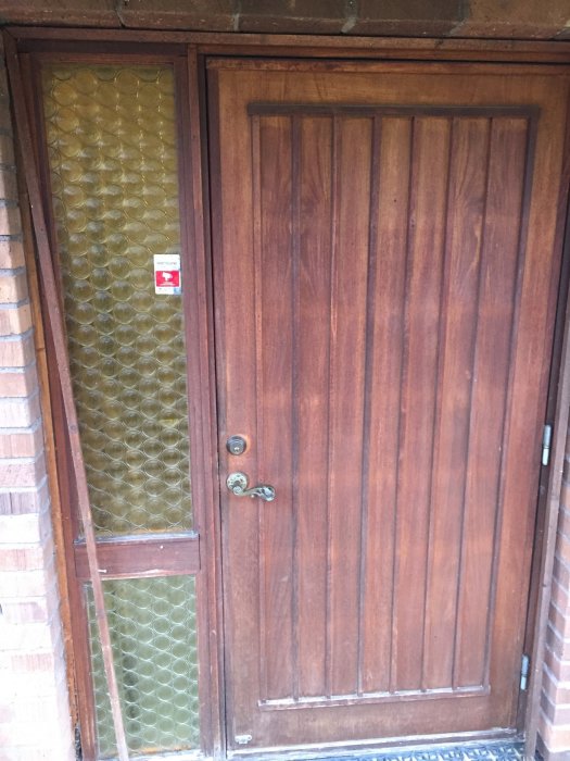 Äldre ytterdörr i trä med glasad sidopanel före renovering.