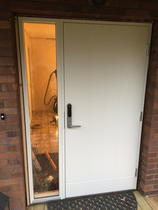 En nyinstallerad vit ytterdörr med glasparti överst, omgiven av tegelvägg och uppställd på en byggarbetsplats.