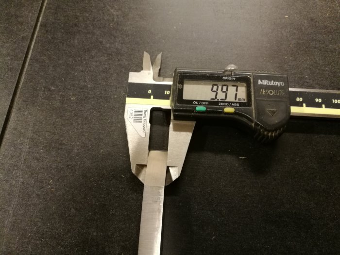 Skjutmått som visar måttet 9,97 mm på ett lockbettelverktyg mot svart bakgrund.