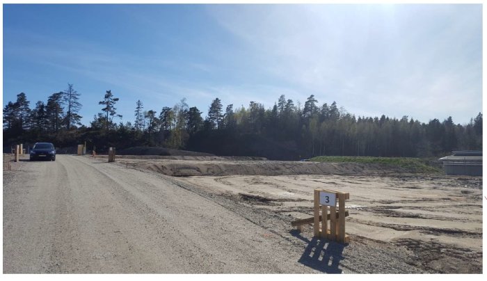 Nybyggnadsområde med utmärkt tomt nummer 3, grusväg och skogsområde i bakgrunden.