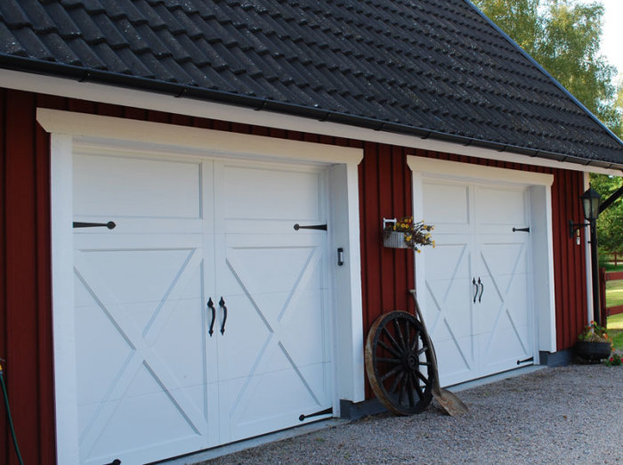 Två vita garageportar med kryssmönster på en röd trävägg, nära markhöjd på en cementplatta.