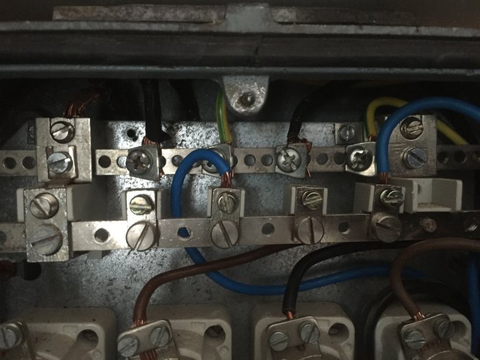 Översikt över en gruppcentral med synliga kopparskenor och elektriska ledningar, några anslutna med slitslagna skruvar.