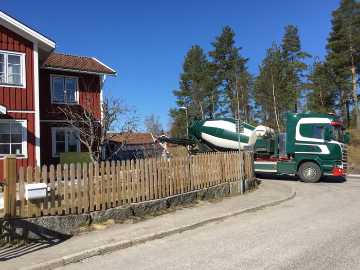 Betonbil framför rött hus gjuter grund för uterum under en solig och blåsig dag.