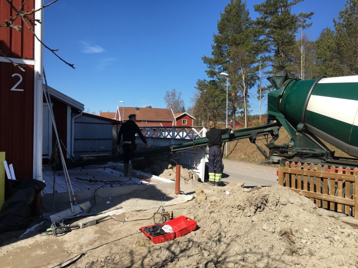 Arbetare gjuter en betongplatta för ett uterum med hjälp av en betongbil under en solig dag.