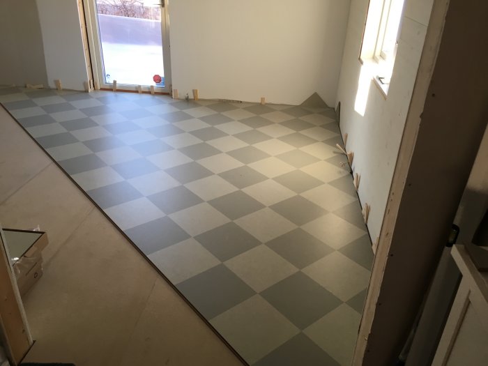 Nyinstallerat Marmoleum click-golv med schackrutigt mönster i ett rum under konstruktion.