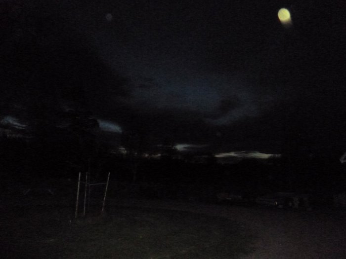 Tidig morgonhimmel fotograferad klockan fyra, med mörka moln och svagt ljus i horisonten över en trädgård.