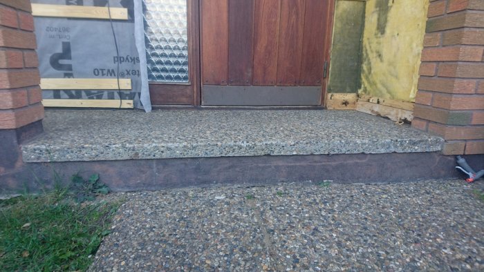 Upphöjt entreparti framför ytterdörr klädd med dansk sjösten, intill renovering på gång.