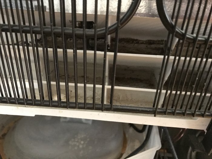 Föroreningar och smuts bakom element i radiator, synliga genom metallstänger framför grå bakgrund.