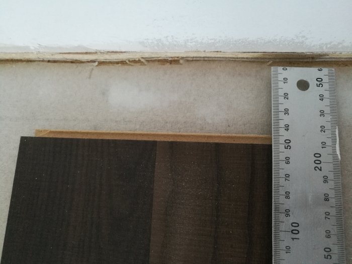 Måttstock bredvid en icke slutförd vägg och golvskarv i ett byggprojekt.