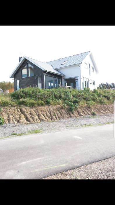 Hus med altan och omgivande oönskad vegetation på tomten, synligt ogräs under altanen.