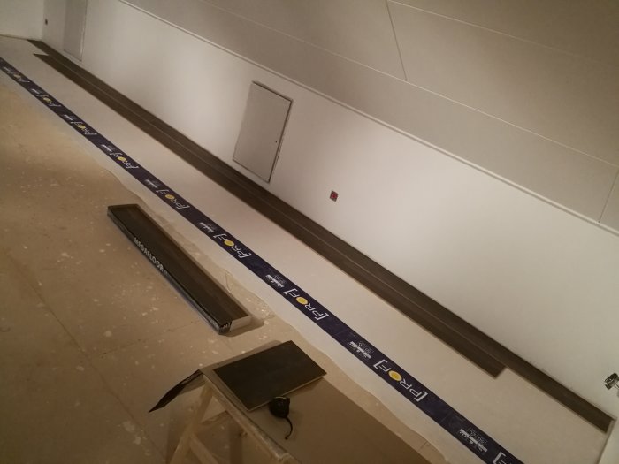 Renoveringsarbete inomhus med golvlister, täckskenor, verktyg och skyddstejp på golvet.
