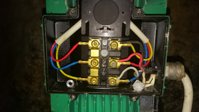 Interiör av en elektrisk pumpkontrollpanel med färgkodade ledningar och anslutningar.