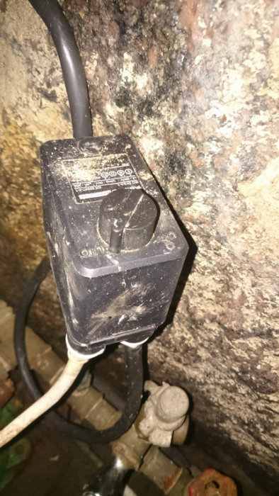 Skitig svart strömbrytarlåda märkt "AUTO-OFF" monterad på en vägg med sladdar och rör i bakgrunden.