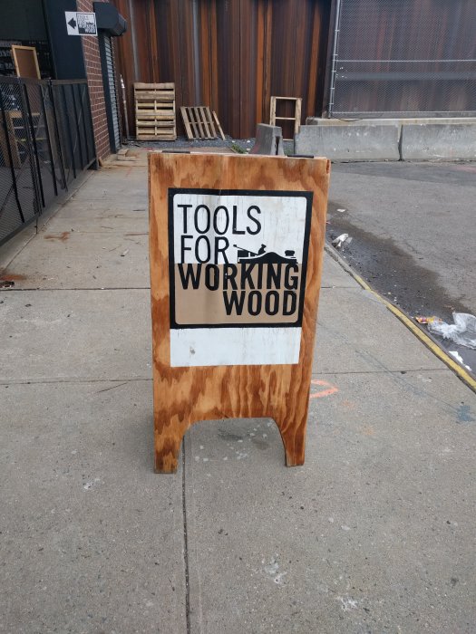 Skylt som säger "TOOLS FOR WORKING WOOD" utanför en butik på en stads trottoar.