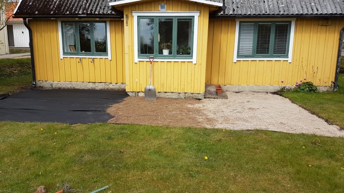 Markduk och bärlager utlagt som grund för ny altan vid gul trähusfasad.