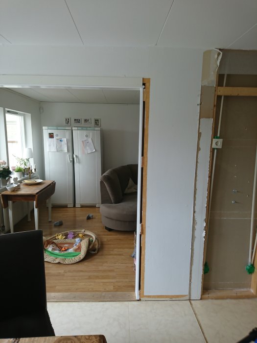 Renoverad bostad med avlägsnade väggsektioner, synlig stomme och kylskåp placerat i vardagsrum.
