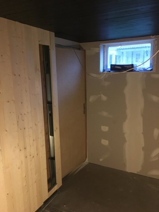 Renovering av ett mansrum med nytt träpanel och spacklade väggar i källaren.