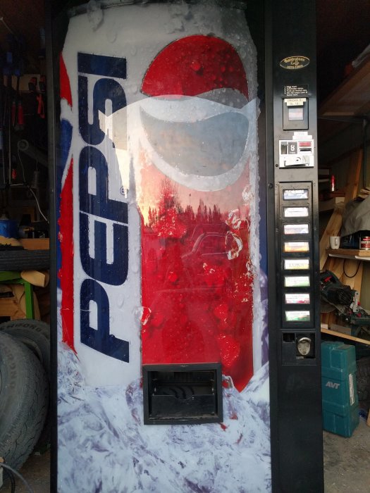 En gammal Pepsi-läskautomat täckt med is och snö i ett garage.