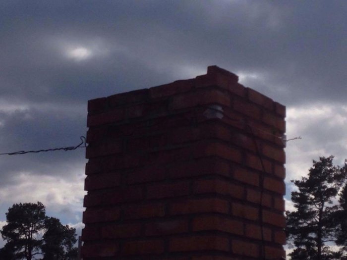 Skorstensspets med lösa tegelstenar mot en molnig himmel, problematisk för installation av ny bula.