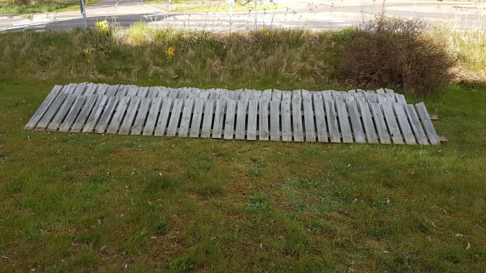 Nedplockat gammalt trästaket som ligger på gräsmattan i väntan på återanvändning eller målning.