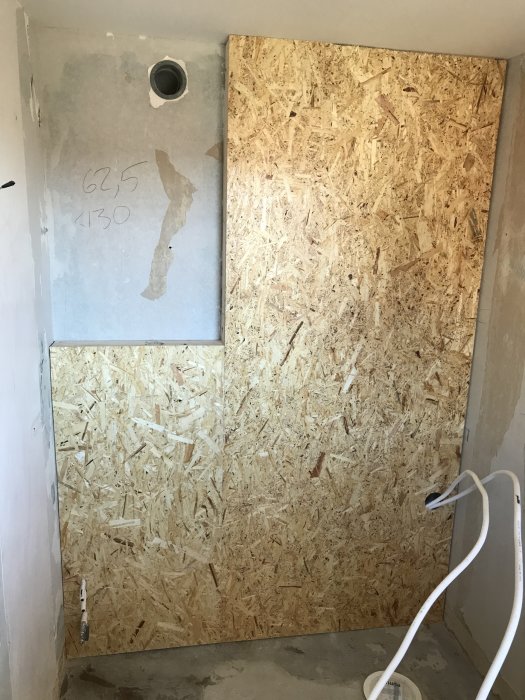 OSB-skivor installerade på vägg i en badrumsrenovering med synliga rör och mätmarkeringar.