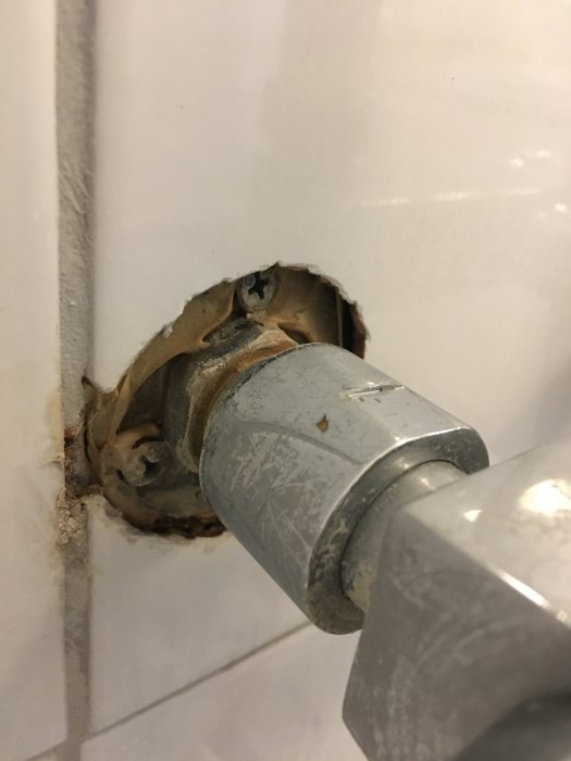 Vit kakelvägg, skadad kakelfog, exponerad rörinstallation, inbäddad rörända, behov av underhåll/reparation.