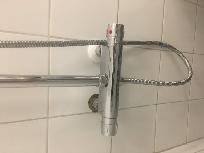 Duschhandtag och slang monterade på kakelvägg i badrum, med röd temperaturmarkering.