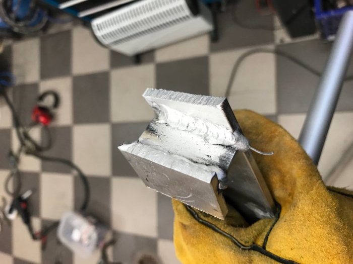 Aluminiumprofil hållen i en skyddshandske med en synlig MIG-svetsfog som illustrerar svetskvalitet på tjock plåt.
