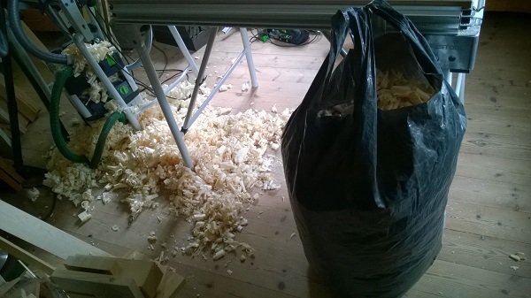 Golv täckt med träspån och en svart sopsäck fylld med spån i ett arbetsrum.