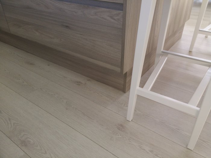 Ljus trägolv och köksinredning med vit stol och skåp.