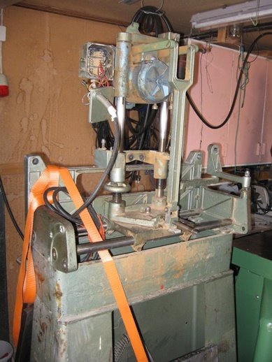 En gammal, sliten vertikalfräs i behov av renovering, med synliga sladdar och säkerhetsspännband runt basen.