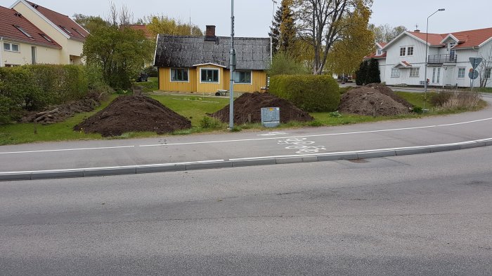 Ett gult hus med en trädgård där det pågår grävarbete, synliga högar av jord och en brandpost framför huset.