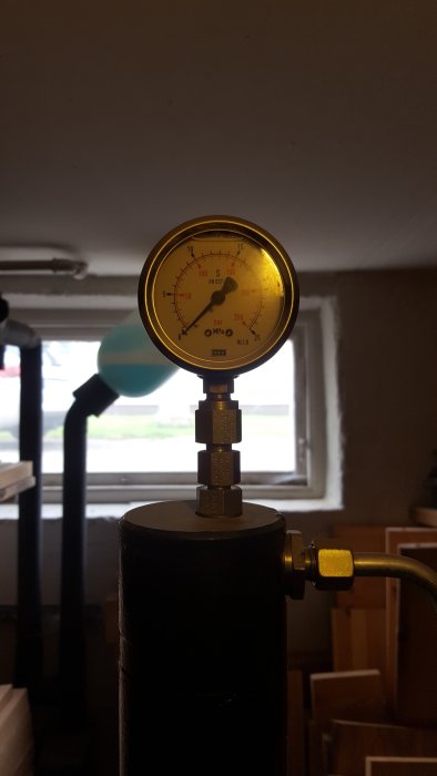 Manometer på toppen av en svart hembyggd press mot en bakgrund av ett fönster och vägg.