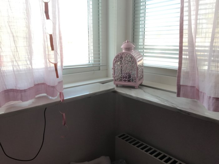 Intakt fönsterbänk med rosa lanterna, vita persienner och lila gardin mot en ljus vägg.