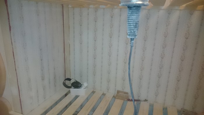 Ombyggt rum med sovalkov, visande en vägg med blommig strukturtapet och ojämn yta vid kanterna, samt en slipmaskin på golvet.