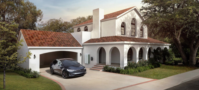 Vit villa med terrakottafärgade soltakpannor, Tesla-bil och laddstation framför garaget.