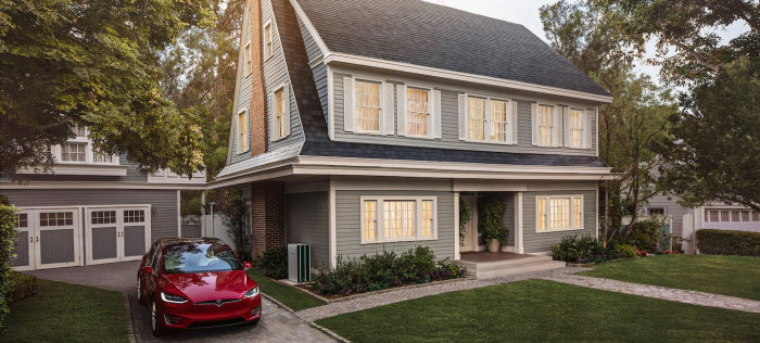 Hus med soltakpannor som passar designen, Tesla-bil framför garage.