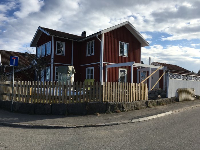 Snickare justerar stomme på bygge vid röd trävilla med felaktiga ytterhörnstolpar.