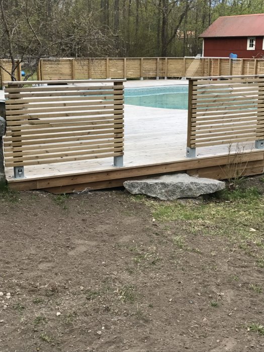 Nyinstallerat staket runt en trall med utsikt över en pool, väntande på oljebehandling, med skog i bakgrunden.