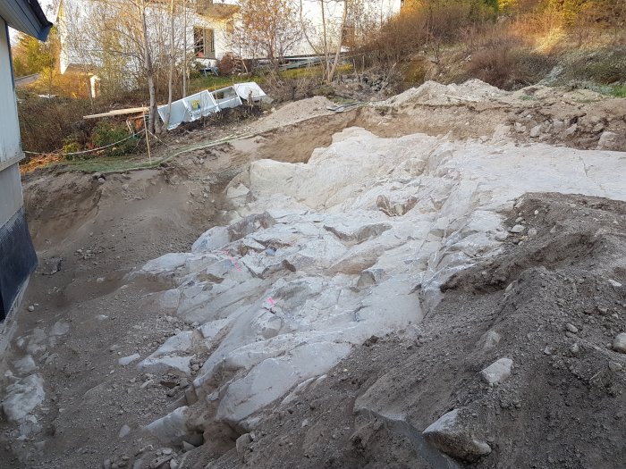 Förberett område för pool vid en husvägg med utgrävd och sprängd berggrund samt markerade gränser.