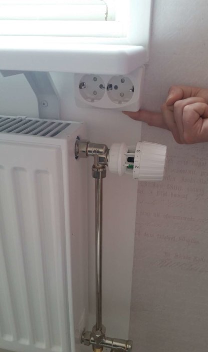 Eluttag monterat under en fönsterbräda med synlig matning och en radiatorventil undertill.