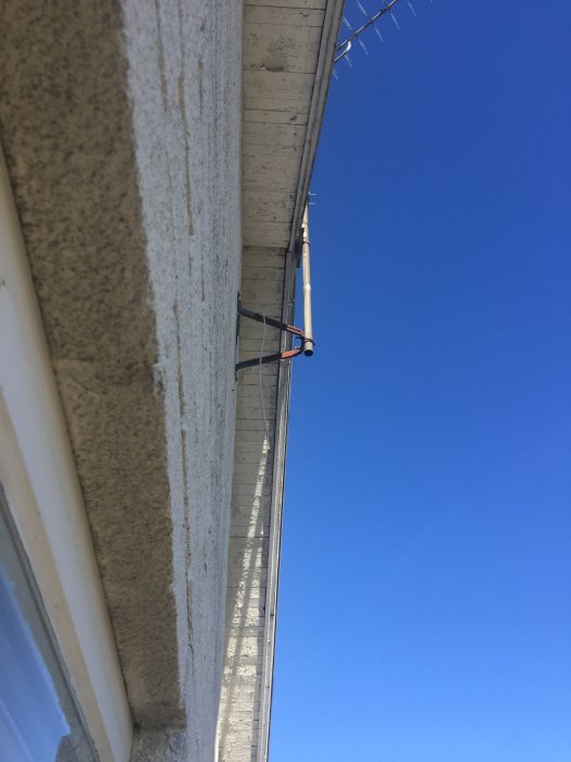 Låg vinkelvy av hus med blottade träkonstruktioner under taköverhänget mot en klarblå himmel.