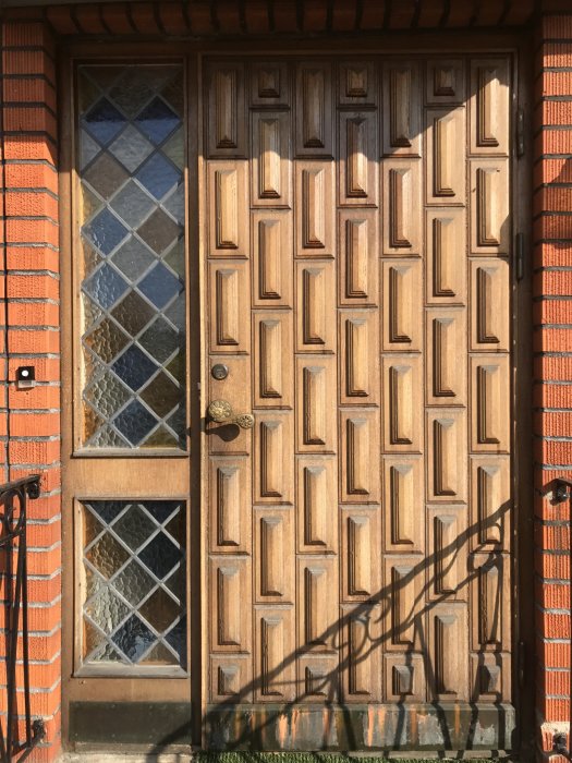 Sliten trädörr med geometriskt mönster från -62, intill fönster med blyinfattat glas.
