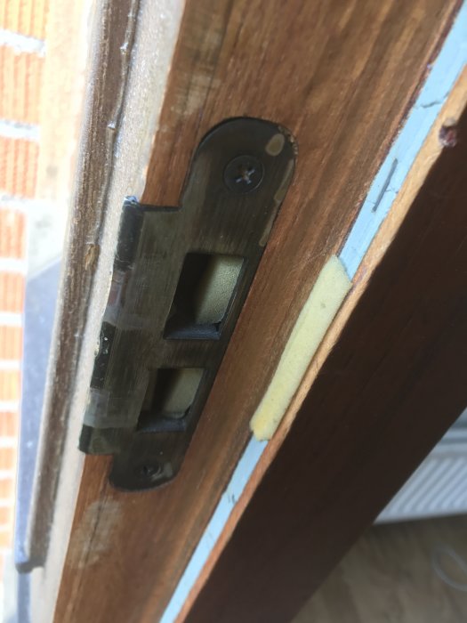 Närbild av en gammal sliten dörrlåsmekanism i en träytterdörr som behöver renovering.