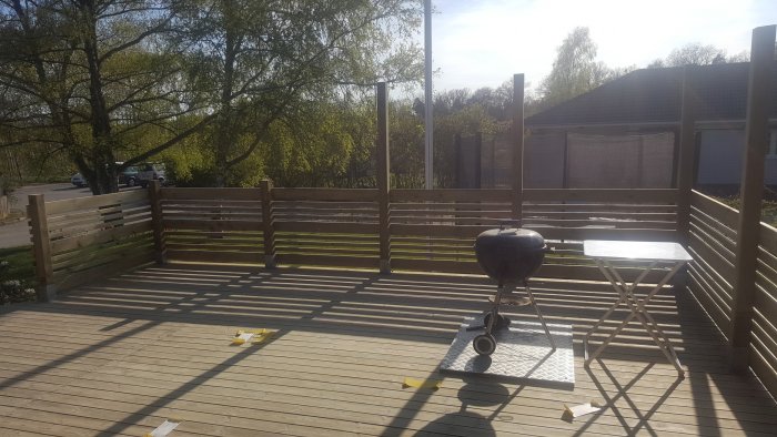 Trädäck med ett ofullständigt ribbstaket och metallstolpar utan överliggare.