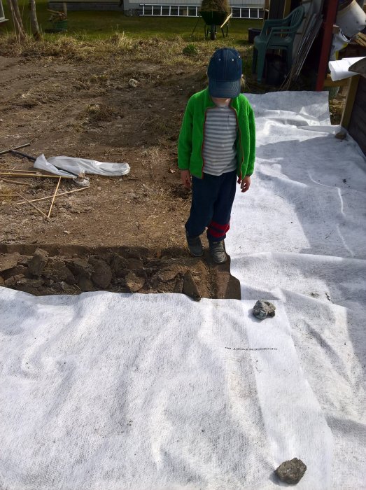 Barn står på vit markduk bredvid nygrävd jord i trädgården inför utplantering.