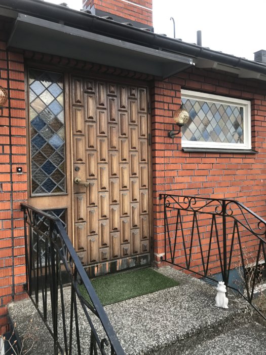 Gammal träytterdörr med mönster och snidade detaljer i behov av renovering, monterad i tegelhus.